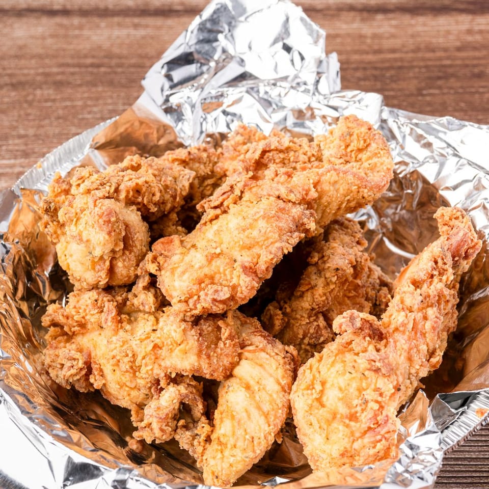 Crispy fried chicken tenders in a foil-lined container on a wooden table.