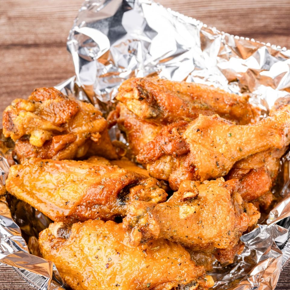 Golden-brown chicken wings in a foil container on a wooden surface.
