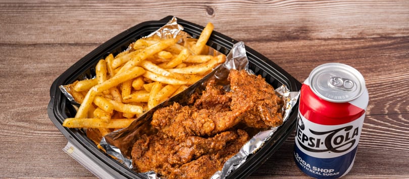 Crispy fried chicken tenders and seasoned fries in a black takeout container with a Pepsi-Cola can.